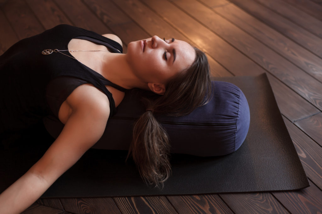 Woman resting after a yoga class in shavasana. Under back her bolster for spine therapy